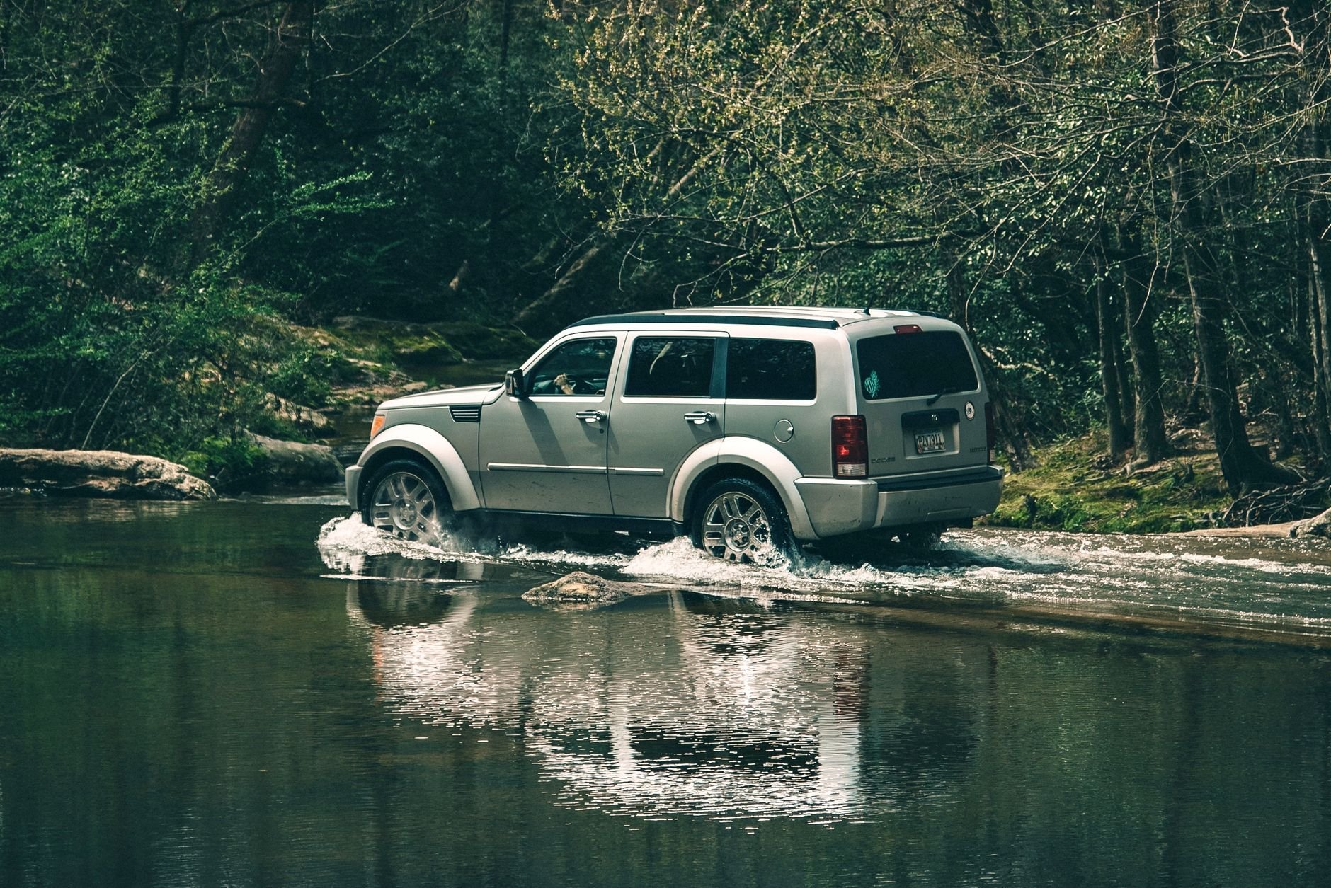Silver SUV crossing a shallow river in dense forest